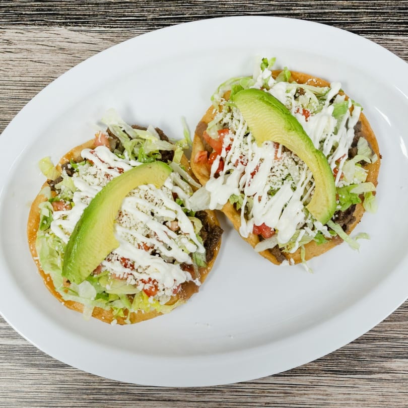 Two tostadas topped with meat, lettuce, tomatoes, cheese, sour cream, and avocado slices.