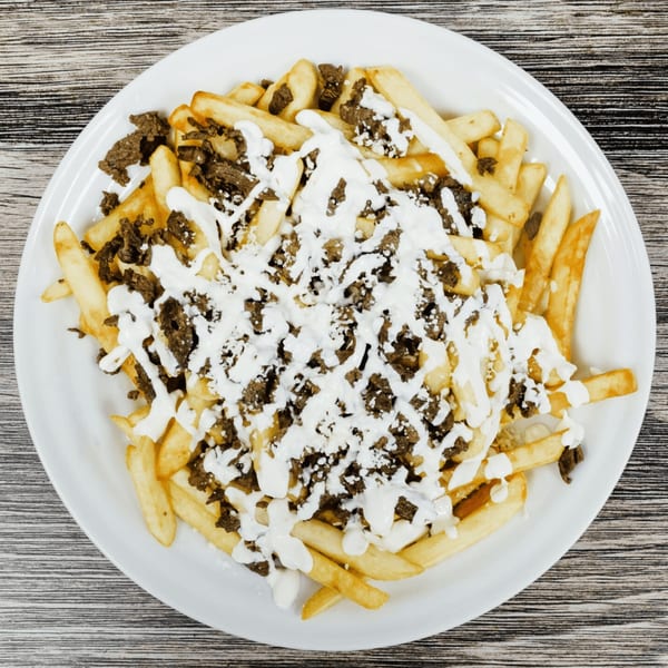 Golden french fries topped with seasoned meat and drizzled with white sauce on a white plate.