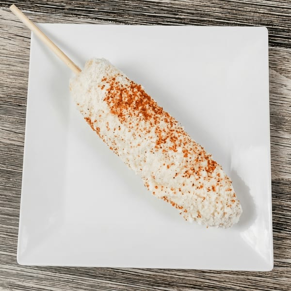 Elote, Mexican street corn, on a stick, covered in white cheese and red chili powder.