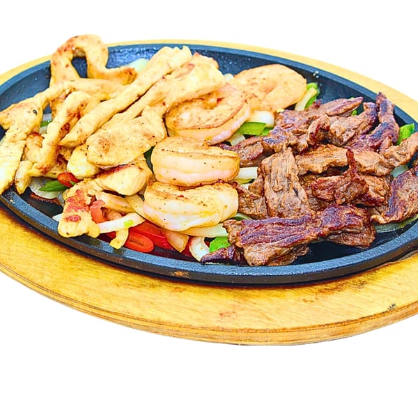 Sizzling fajitas with chicken, shrimp, and steak, served on a cast iron platter.
