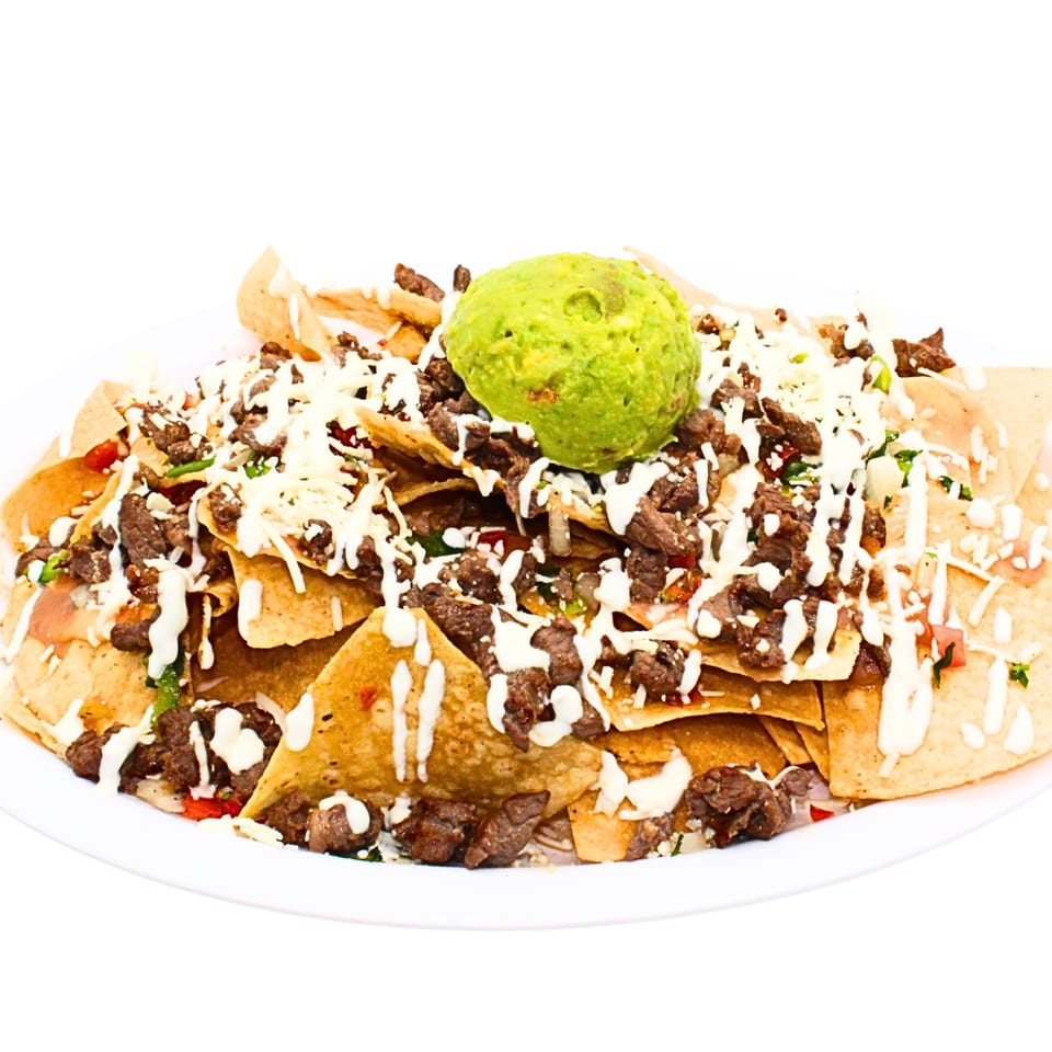 Loaded nachos with steak, shredded cheese, white sauce, and a large scoop of guacamole.