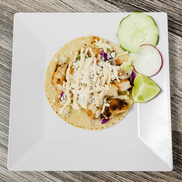 A shrimp taco with sauce, cheese, and cabbage, served with cucumber, radish, and lime.