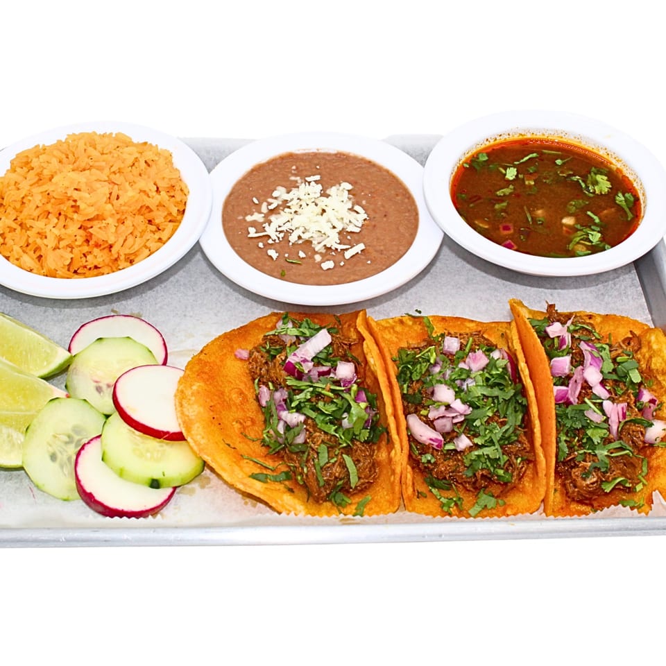 Three birria tacos with rice, beans, consommé, and fresh garnishes on a tray.