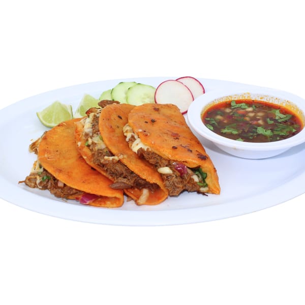 Four birria tacos with melted cheese, cilantro, onions, lime, cucumber, radish, and a side of consommé.
