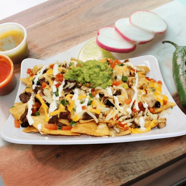 A white rectangular plate of loaded nachos with guacamole, sour cream, and various toppings.