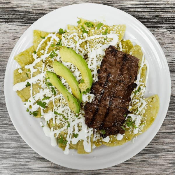 Chilaquiles with green sauce, grilled steak, avocado slices, sour cream, and crumbled cheese.