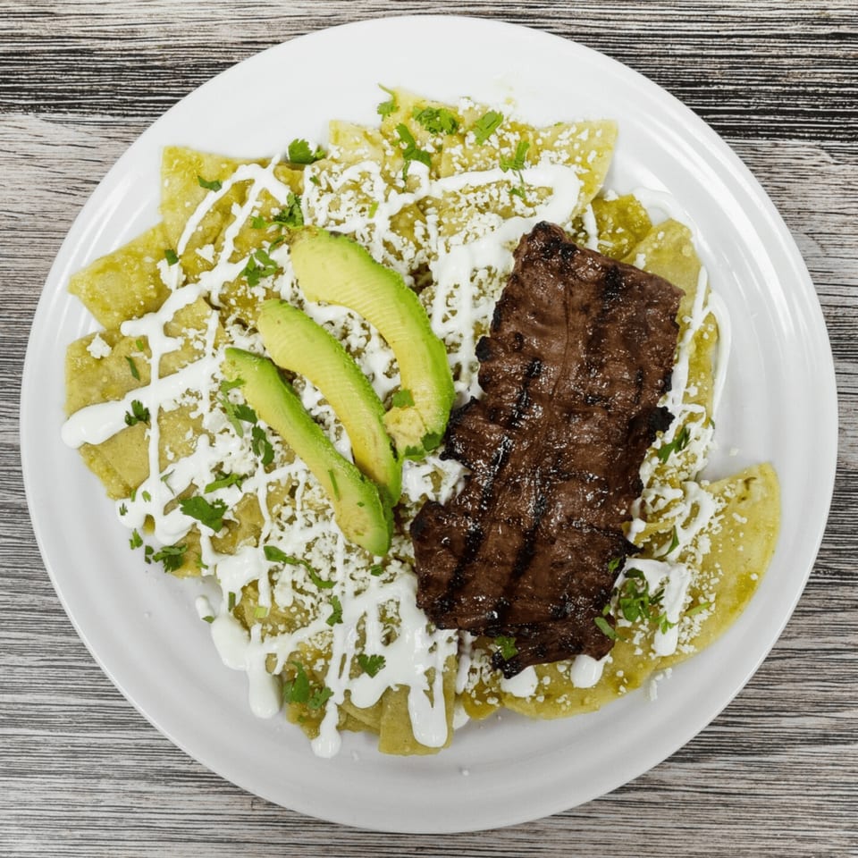 Chilaquiles with green sauce, grilled steak, avocado slices, sour cream, and crumbled cheese.